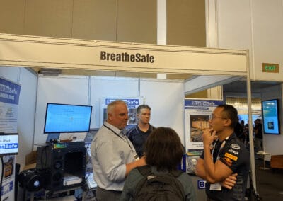 High-voltage bottled helium filtration and pressure solutions by BreatheSafe at a trade show booth with attendees discussing respiratory safety systems.