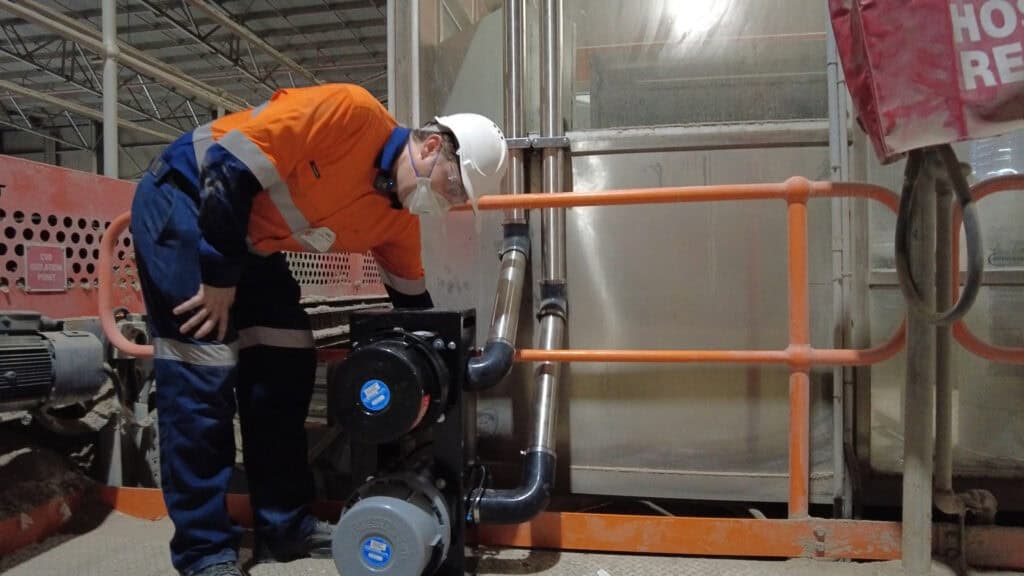 High-visibility worker inspecting industrial ventilation system for safety and air quality in a factory setting.