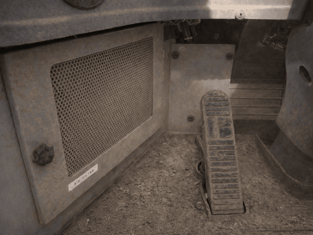 The OEM ventilation system with a metal vent and foot pedal inside a dusty vehicle cab.